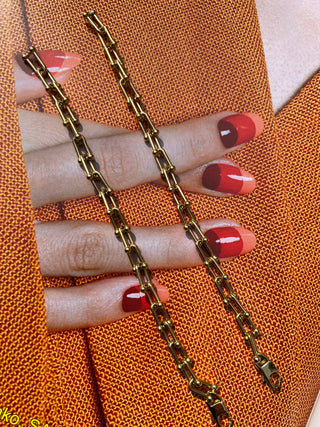 Gold chain bracelet laid over a photo of a hand with red nails and orange fabric. Featured Product: Audrey Bracelet, SKU: BR-21289-001-RG