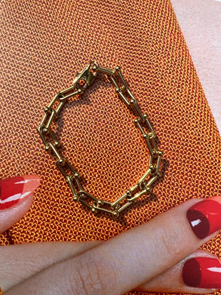Gold chain bracelet on textured brown surface with red nails in frame. Featured Product: Audrey Bracelet, SKU: BR-21289-001-RG