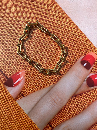 Gold chain bracelet on orange surface beside a hand with red and orange nails. Featured Product: Audrey Bracelet, SKU: BR-21289-001-RG